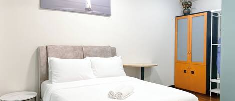 A neatly arranged hotel room with a bed, a small round table, a wardrobe, and a painting of a lighthouse on the wall.