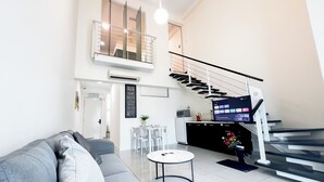 A modern living room with a grey sofa, a small round table, a staircase, and a kitchen area with a TV. - The Scott Garden by Manhattan Group  (Kuala Lumpur)