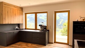 Une cuisine moderne avec des meubles de couleur sombre, un mur d’accent en bois et une grande fenêtre donnant sur un paysage pittoresque.