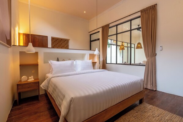 A modern bedroom with a large bed, wooden headboard, bedside tables, and a large window with curtains. - Sofia Villa by Betterplace (Canggu)