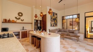 A modern kitchen with a central island, a dining area with a sofa, and a large window with curtains. - Sofia Villa by Betterplace (Canggu)