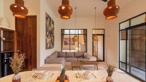 A modern living room with a round dining table set for a meal, a sofa, and a large window. - Sofia Villa by Betterplace (Canggu)