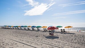 Ein Strand mit Reihen aus Liegestühlen und Sonnenschirmen, von denen einige mit 'FOR RENT' gekennzeichnet sind.