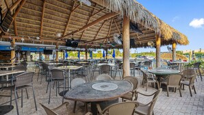 An outdoor dining area with thatched roof, wicker furniture, and a view of the sea. - Condo at the Bay with Resort-Style Amenities, Pool, Tiki Bar (Sarasota)