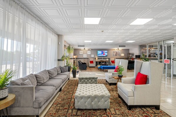 A modern hotel lobby with a grey sofa, a grey armchair, and a patterned carpet.