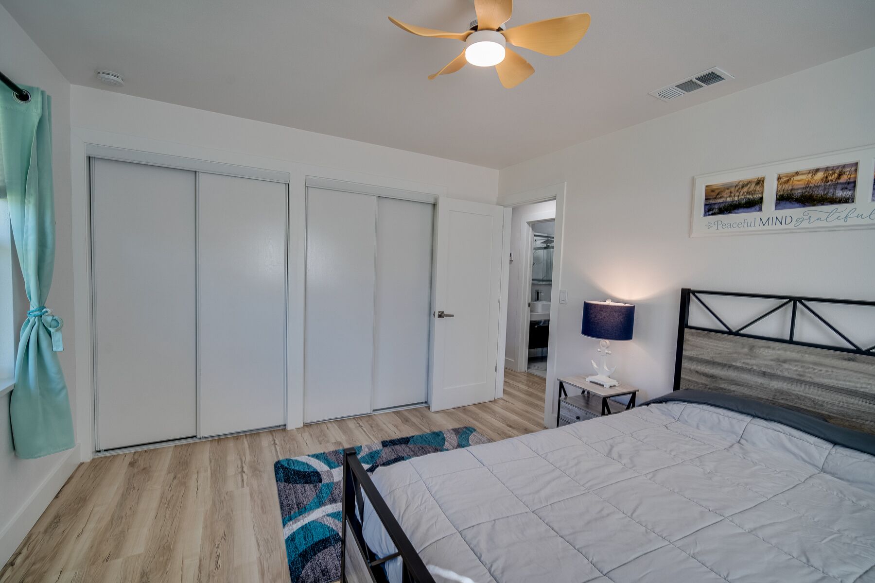 A bedroom with a bed, a ceiling fan, a nightstand, a lamp, and a painting on the wall.