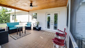 A covered patio with a ceiling fan, outdoor furniture, and a sliding glass door leading to a garden.