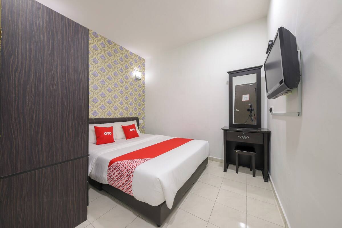 Ein Hotelzimmer mit Bett, Schreibtisch, Stuhl, Fernseher und Kleiderschrank.