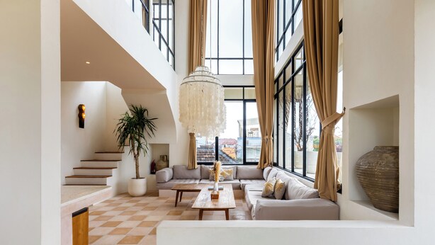 A spacious living area with a high ceiling, a staircase, a large window with curtains, a chandelier, and a large vase. - Leo Villa by Betterplace (Canggu)