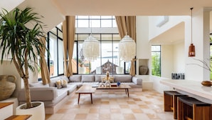 A spacious living area with a large window, a sofa, a coffee table, and a plant. - Leo Villa by Betterplace (Canggu)