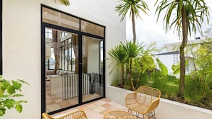 A balcony with wicker furniture, a glass door leading to an interior space, and tropical plants. - Leo Villa by Betterplace (Canggu)