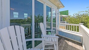 Une terrasse en bois avec des fauteuils Adirondack blancs et un balcon vitré donnant sur un paysage urbain.