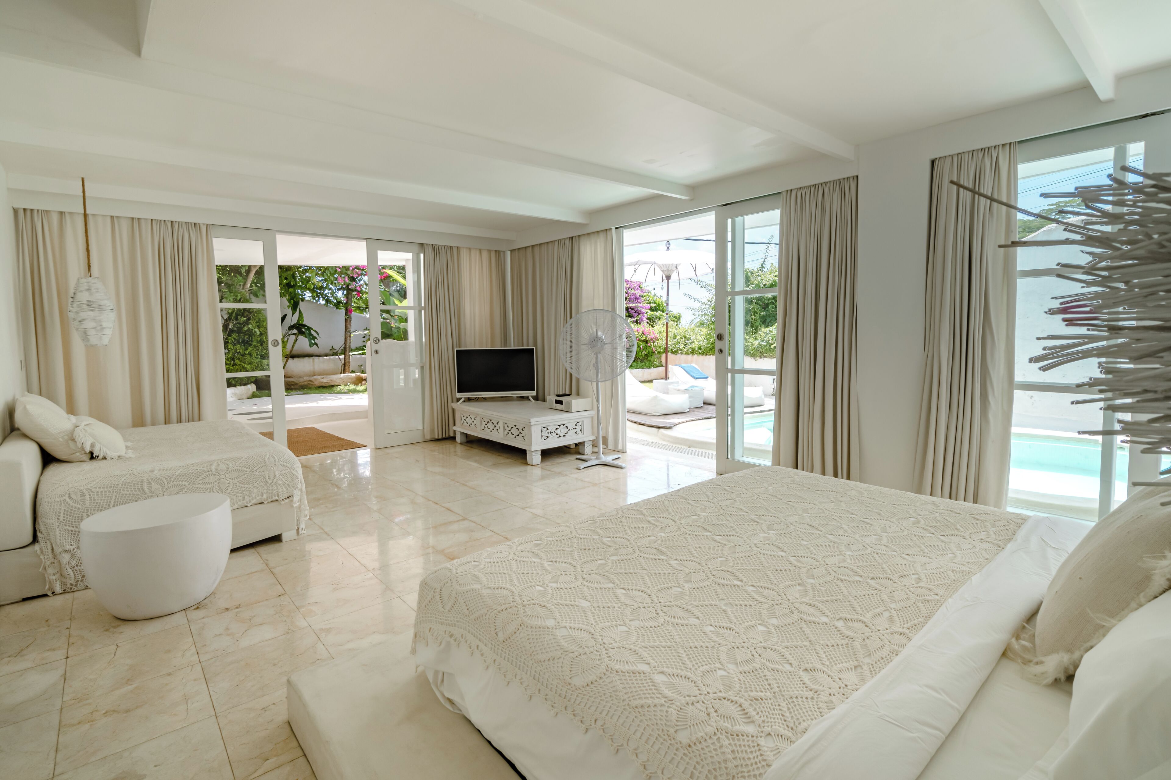 A spacious bedroom with a large bed, a smaller bed, and a seating area. There is a TV and a fan in the room.