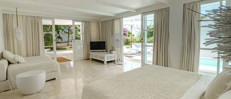 A spacious bedroom with a large bed, a smaller bed, and a seating area. There is a TV and a fan in the room.
