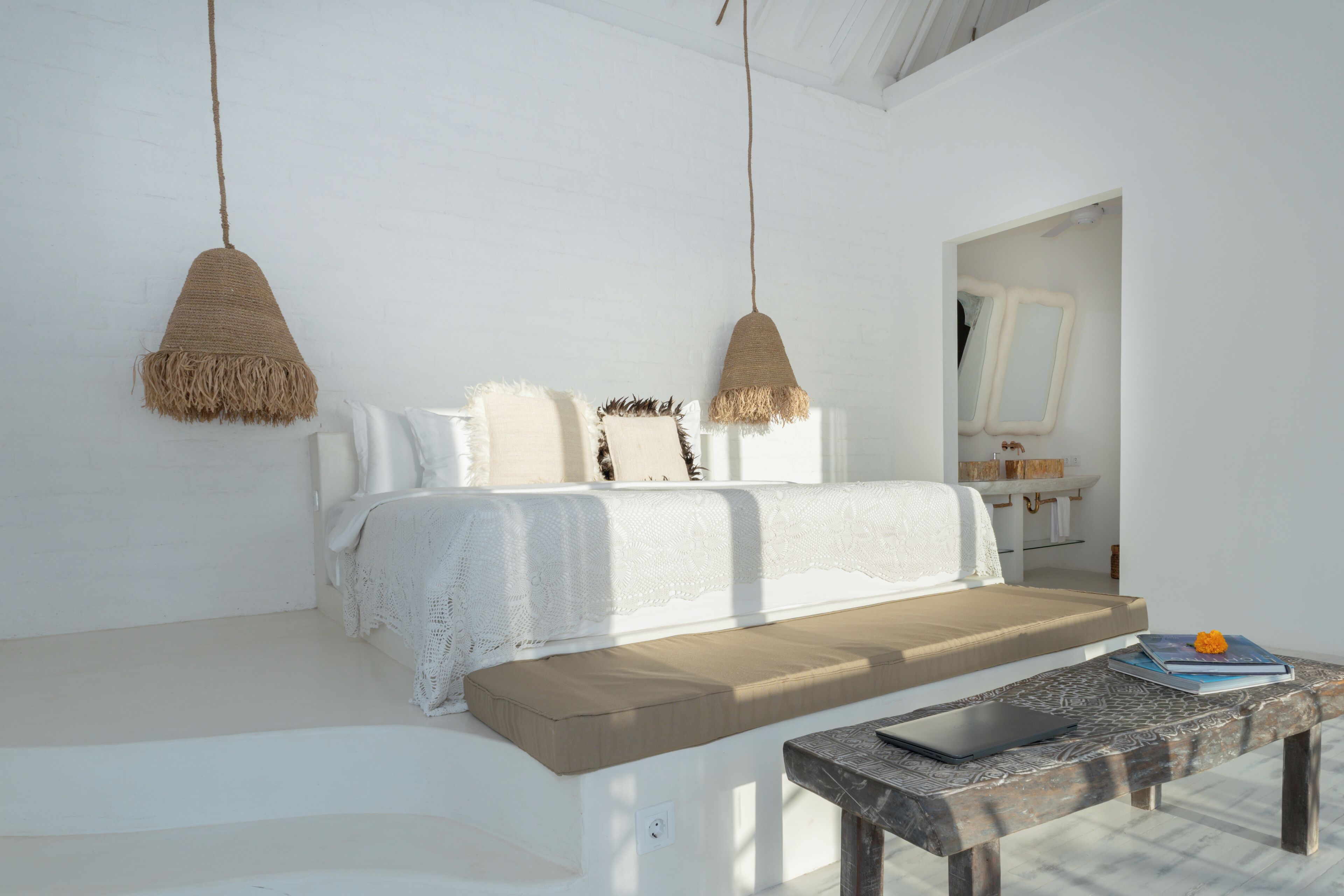 A minimalist room with a white sofa, a wooden bench, and a hanging light fixture.
