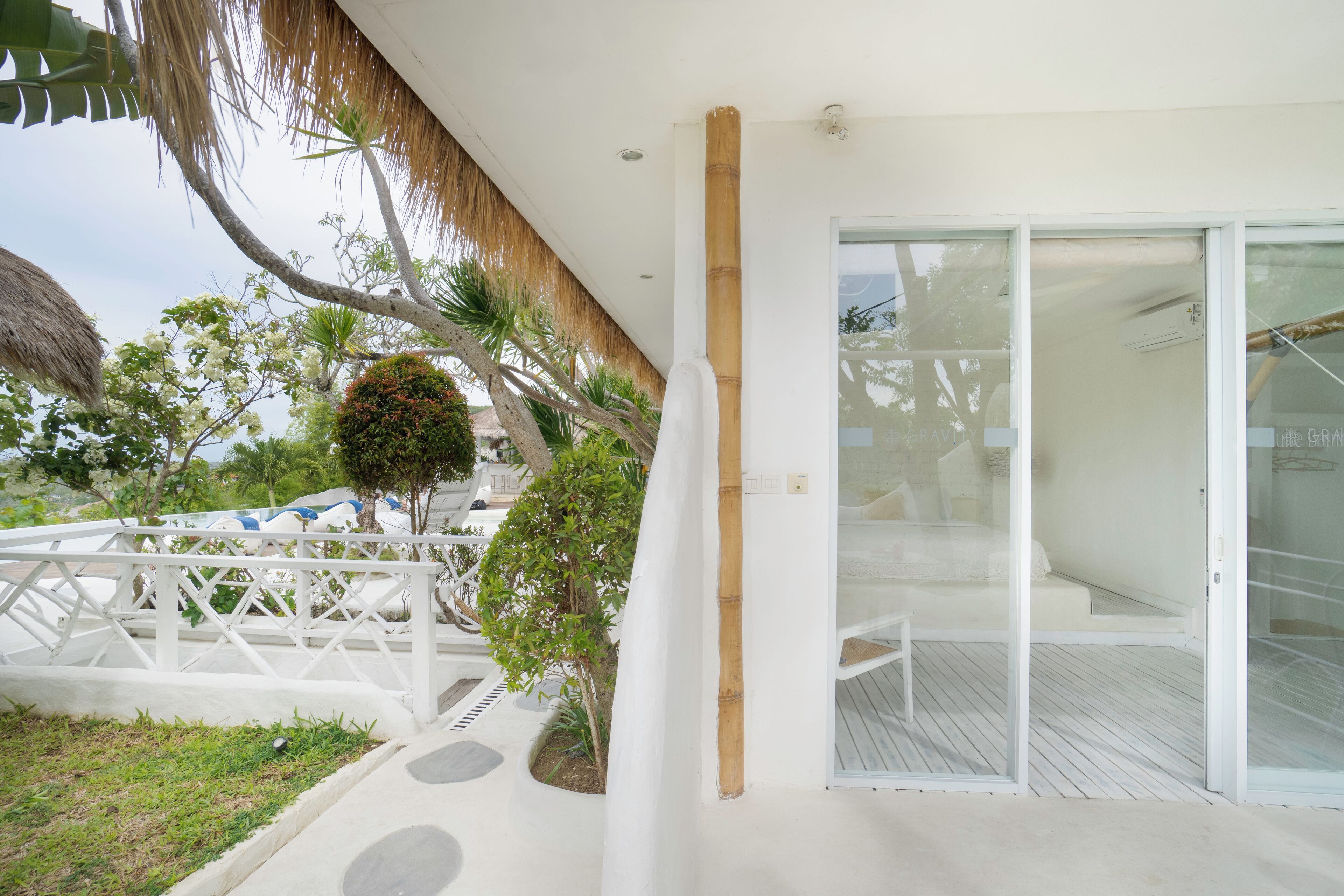 Habitación de hotel moderna con puerta de cristal que da a un balcón, techo de paja y barandilla blanca.