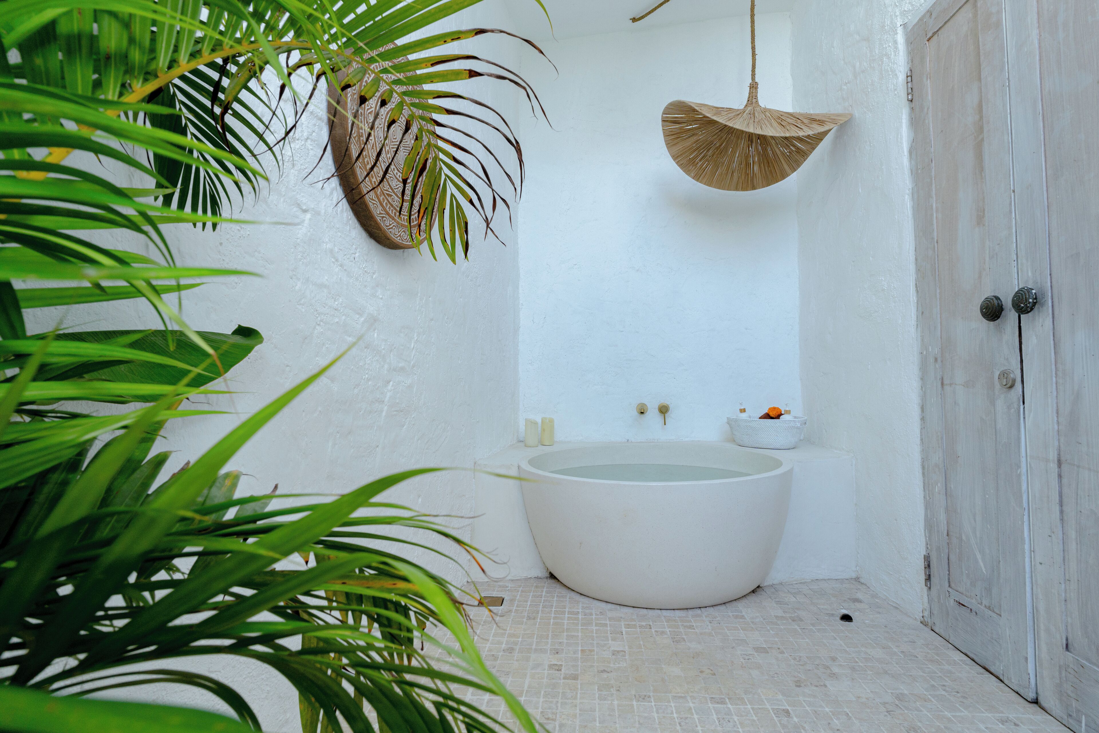 A small, white-walled bathroom with a large bathtub, a hanging basket, and a door.