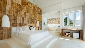 Ein modernes Schlafzimmer mit einem großen Bett, einer Holzwand als Blickfang, einem Badezimmer mit einer Badewanne und einem Schreibtisch mit einem Computer.
