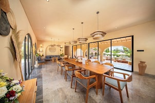 A spacious dining area with a long wooden table and chairs, large windows, and a view of the outdoors.