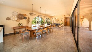 A spacious dining area with a long wooden table and chairs, surrounded by large windows and decorative plates on the walls. - Cabana Kedungu by Ini Vie Hospitality  (Tabanan)