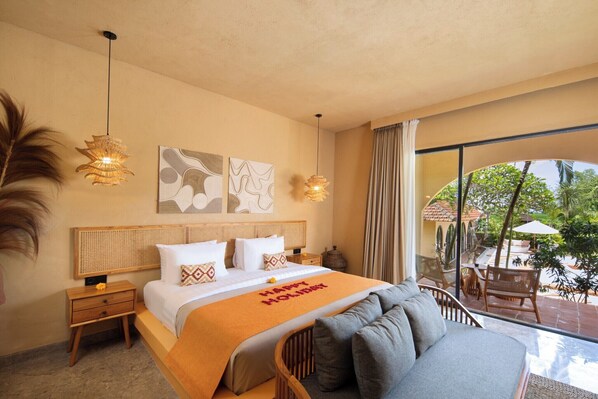 Habitación de hotel con cama, sofá, mesita de noche y un amplio ventanal con vistas al exterior.