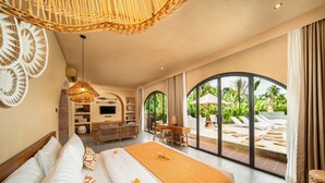 A spacious bedroom with a large bed, a wooden desk, and a view of a lush garden through large windows. - Cabana Kedungu by Ini Vie Hospitality  (Tabanan)