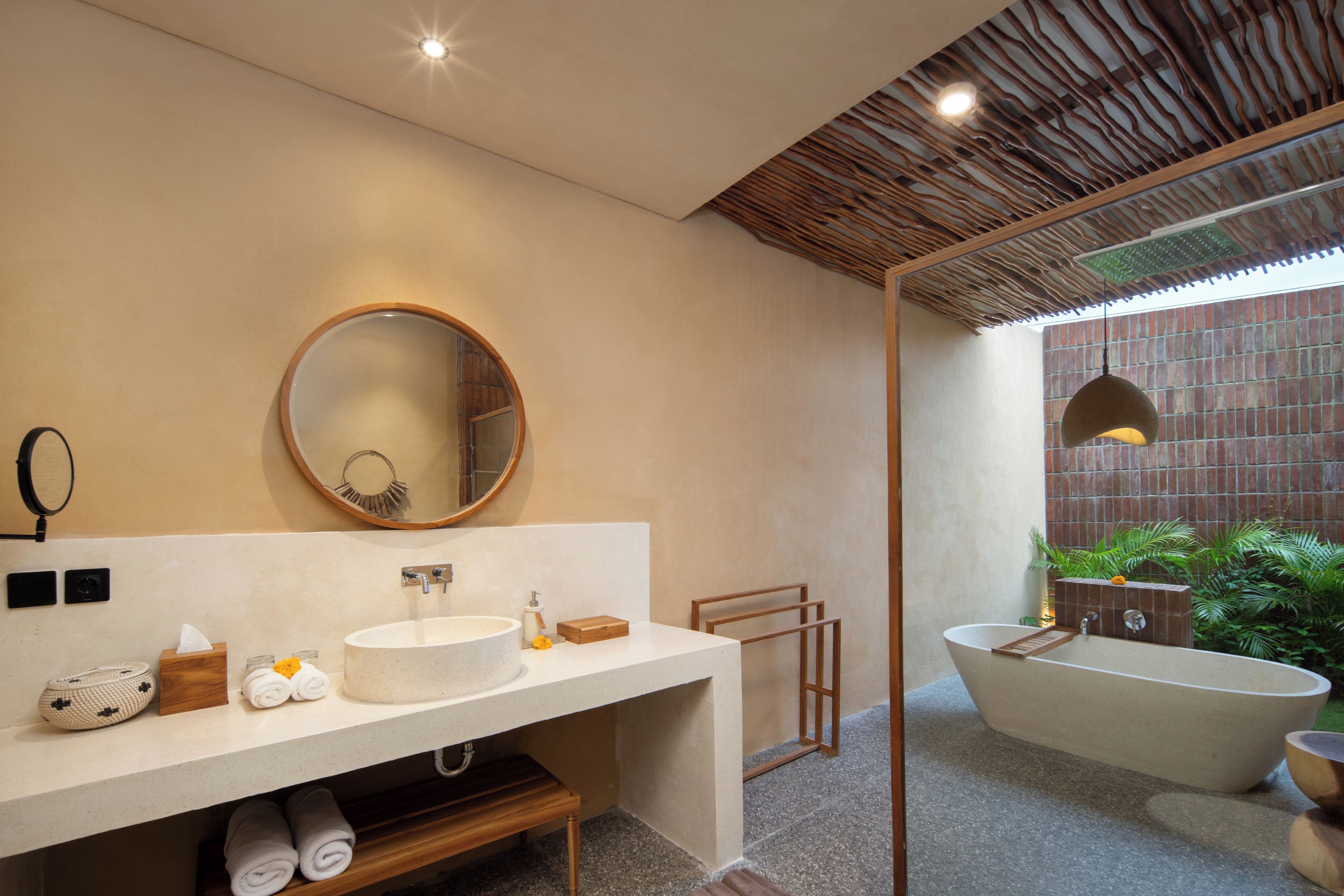 Een moderne badkamer met een grote ronde spiegel, een vrijstaand bad en een houten wastafelmeubel.
