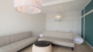 Una sala moderna con un sofá beige, un otoman redondo y una lámpara colgante.