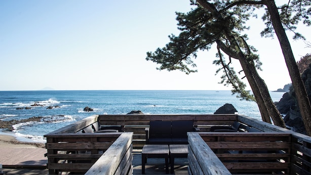 Una terraza de madera con bancos que da a una costa rocosa y el océano.