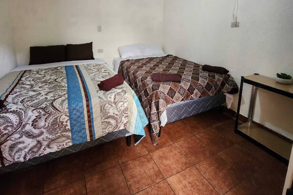 A small, dimly lit room with two beds, a ceiling fan, and a tiled floor.