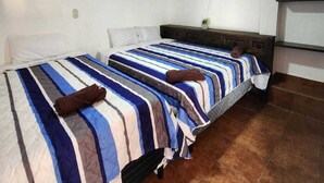 Una habitación con dos camas, techo con diseño de ladrillos, ventilador de pared y una pequeña kitchenette.