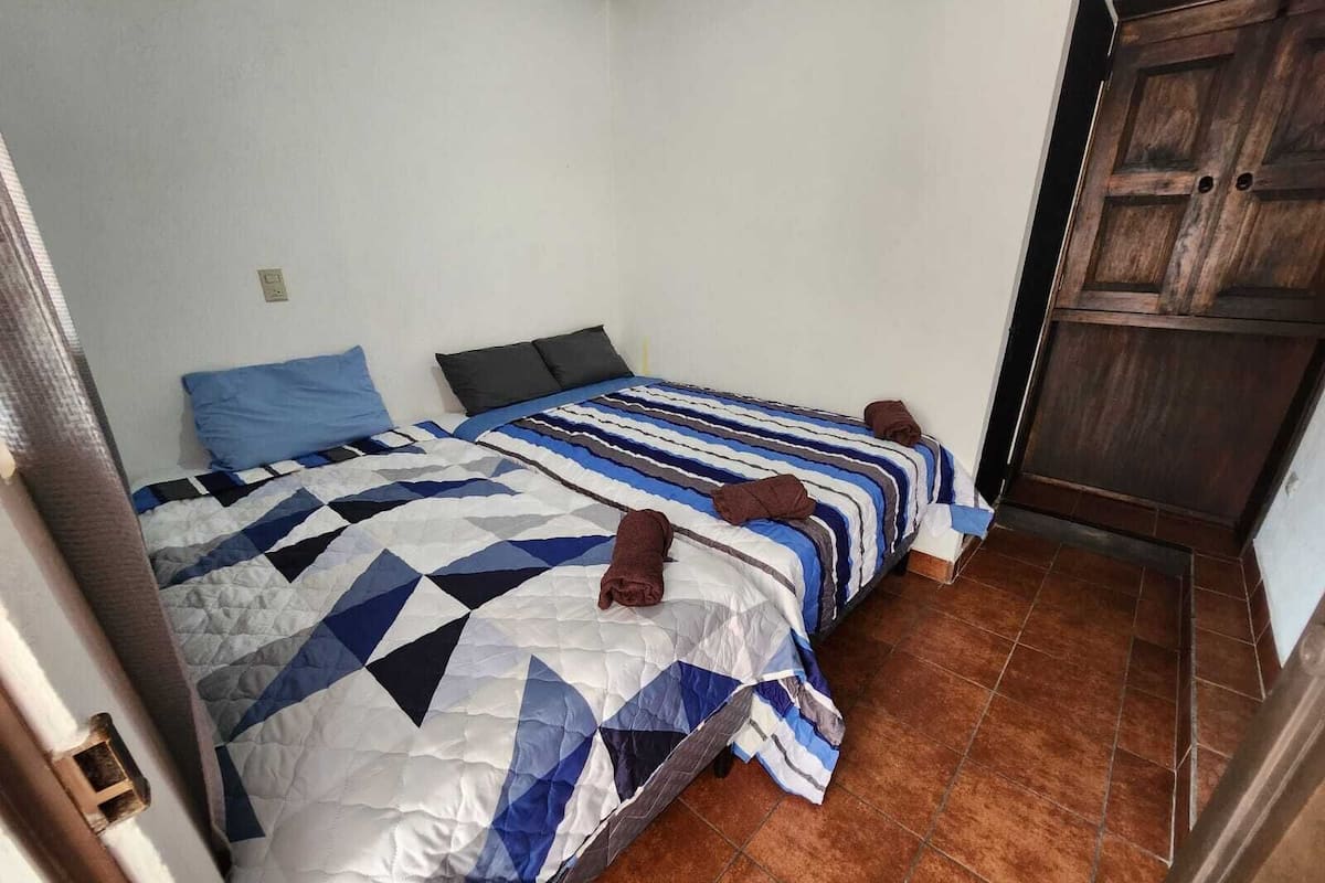 A bedroom with two beds, a wooden wardrobe, and a tiled floor.