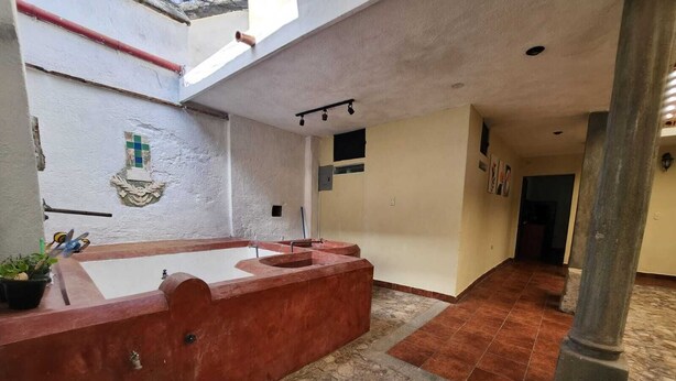 Un espacio interior amplio con una bañera grande, suelo de piedra y un techo alto con tragaluces.