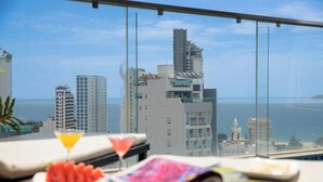 Een hotelkamer hoog in een wolkenkrabber met balkon en uitzicht over de stad en de zee.