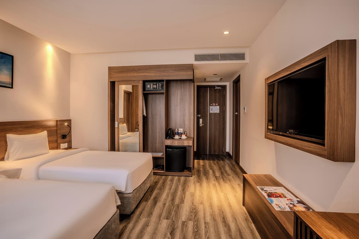 Ein Hotelzimmer mit zwei Betten, einem Fernseher, einer Minibar und Holzboden.