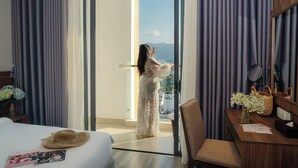 Hotelkamer met een bed, een bureau met een bloevas en uitzicht op bergen door de open deur.