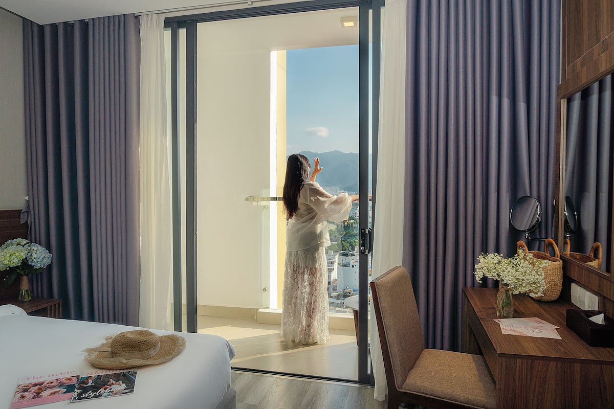 Ein Hotelzimmer mit Bett, Schreibtisch mit Blumenvase und Bergblick durch die offene Tür.