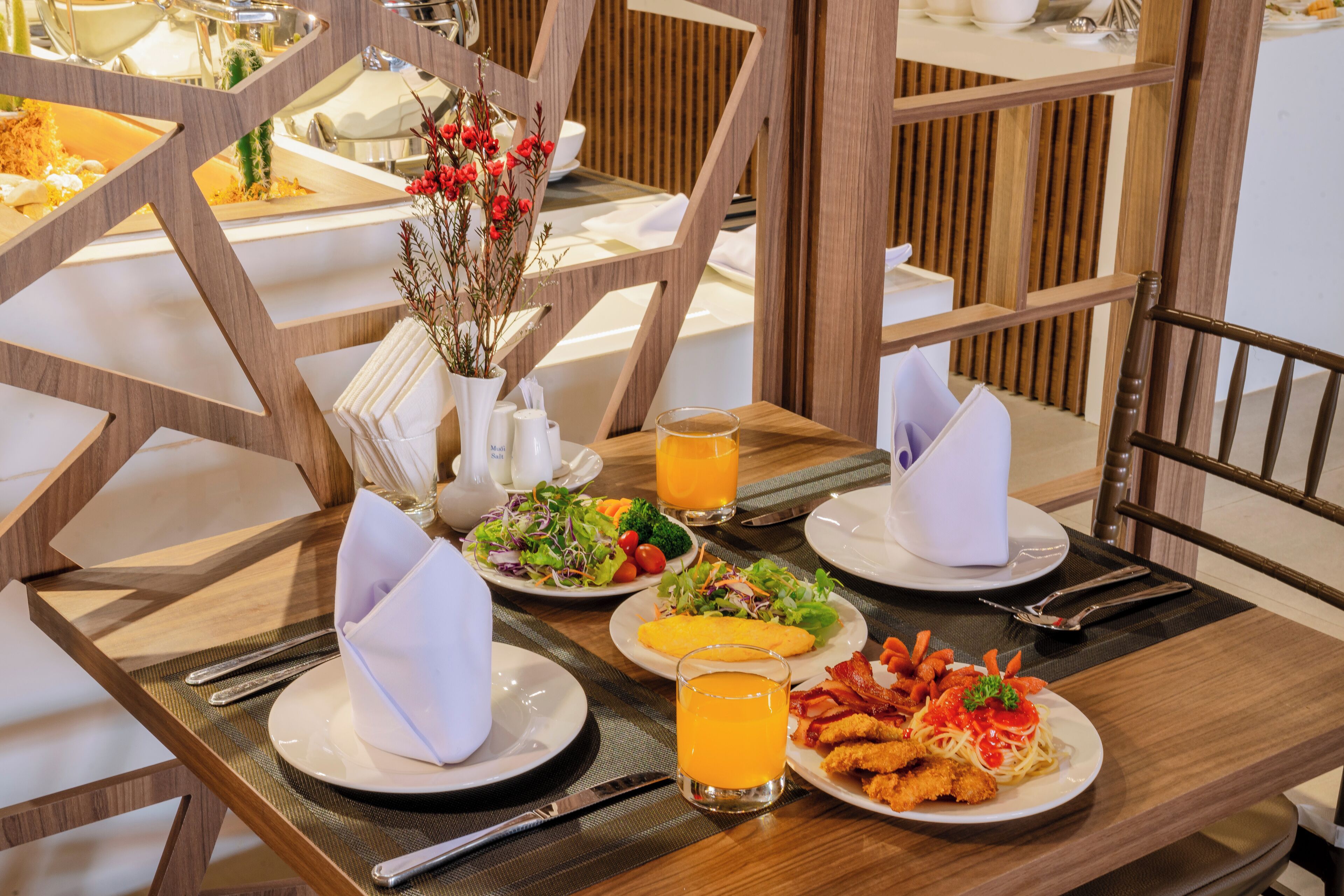 A breakfast buffet with various dishes, including eggs, bacon, and salads, set on a wooden table with a modern design.
