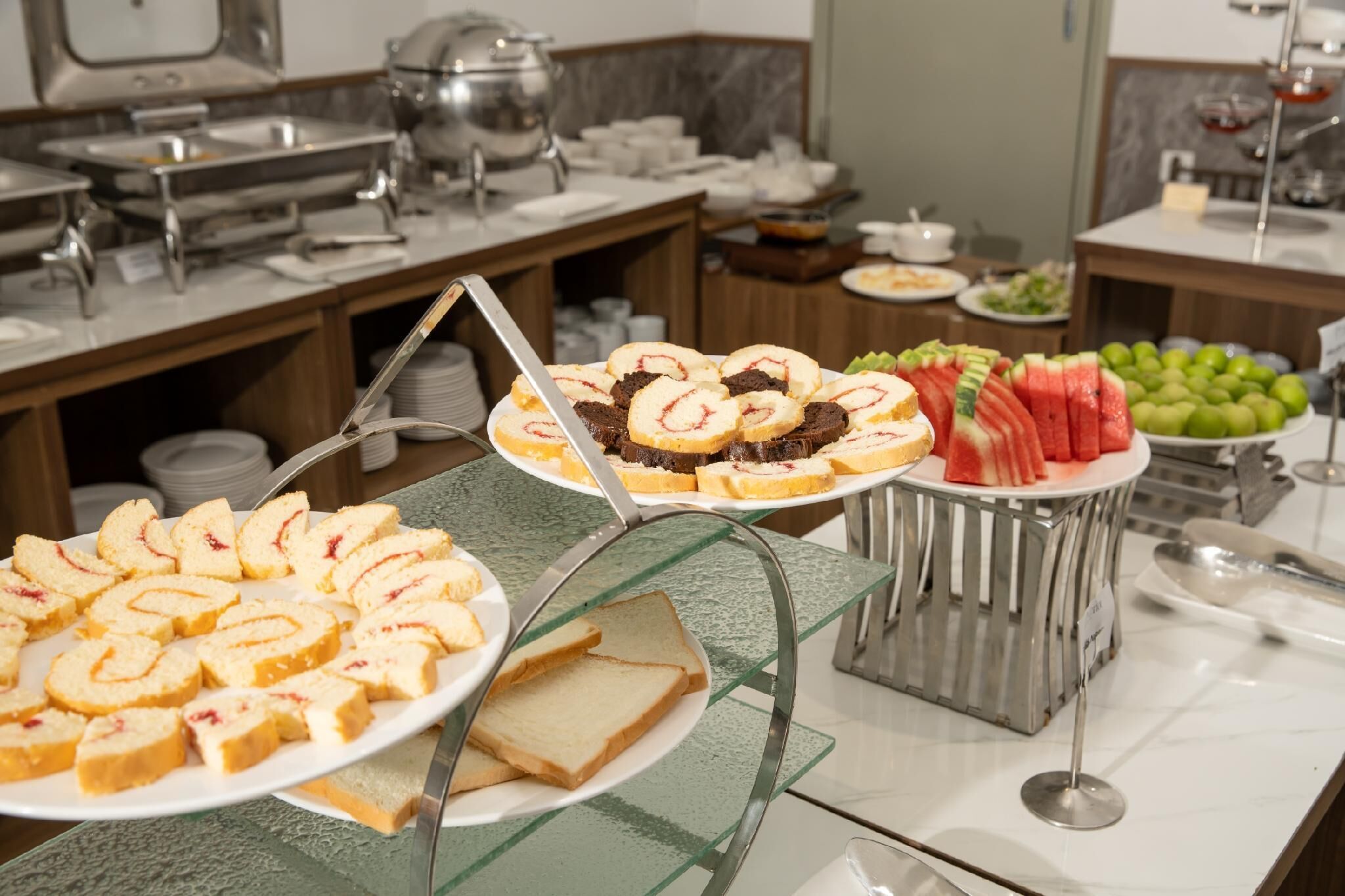A buffet with various food items including sliced bread, cakes, and fresh fruits.