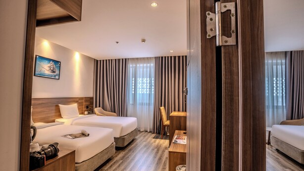 Ein Hotelzimmer mit zwei Betten, einem Schreibtisch, einem Stuhl und einem großen Fenster mit Vorhängen.