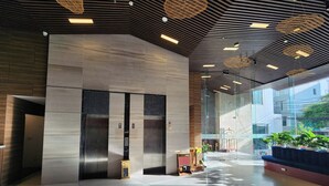 Een moderne lobby met een centrale lift, grote ramen en een plafond met hangende verlichtingsarmaturen.