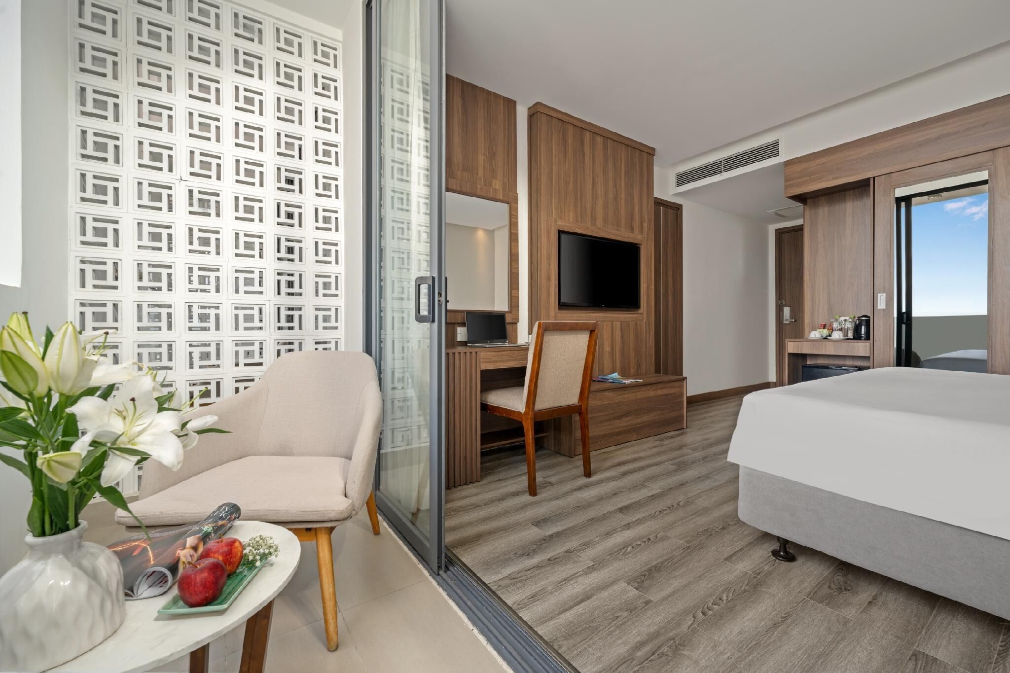 A hotel room with a bed, a desk, a TV, and a seating area with a vase of flowers.