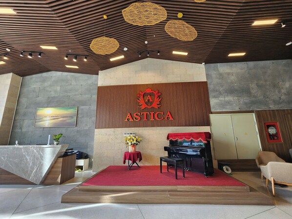 Zona de recepción con un piano, una alfombra roja y el logotipo de ASTICA.