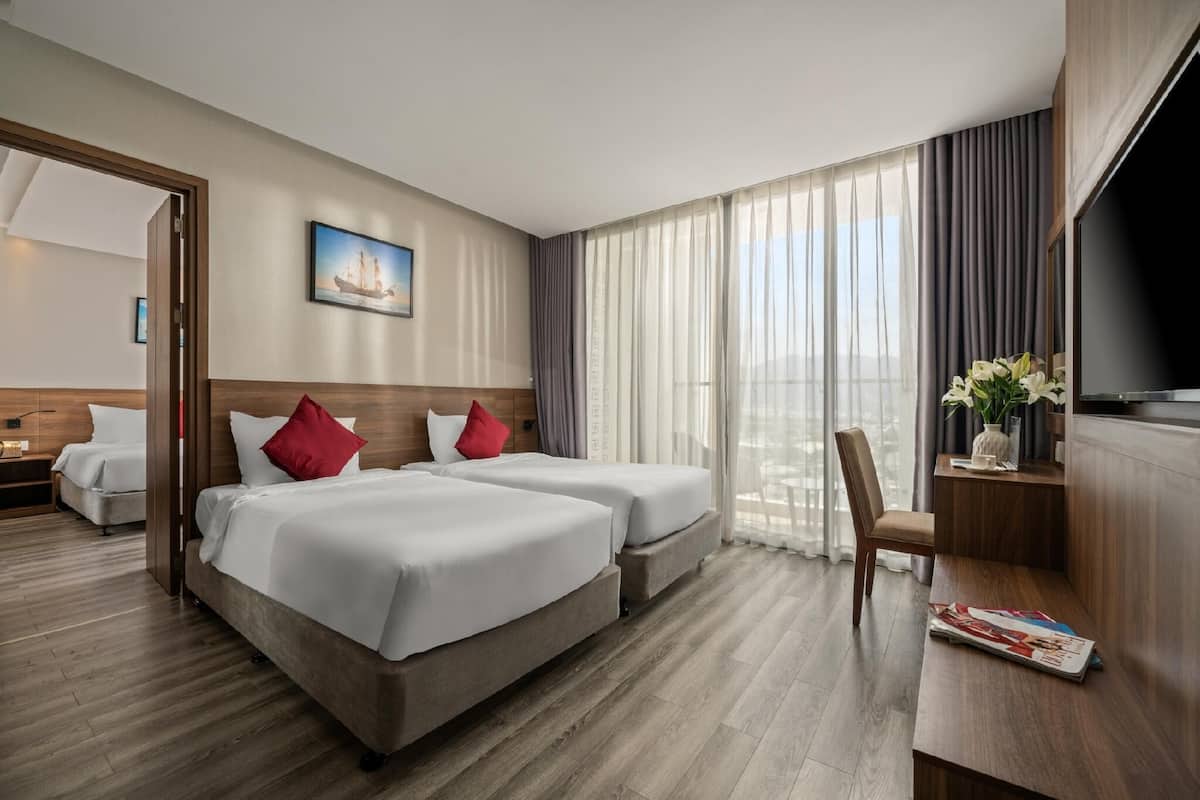 Ein Hotelzimmer mit zwei Betten, einem Fernseher, einem Schreibtisch und Blick auf die Stadt.