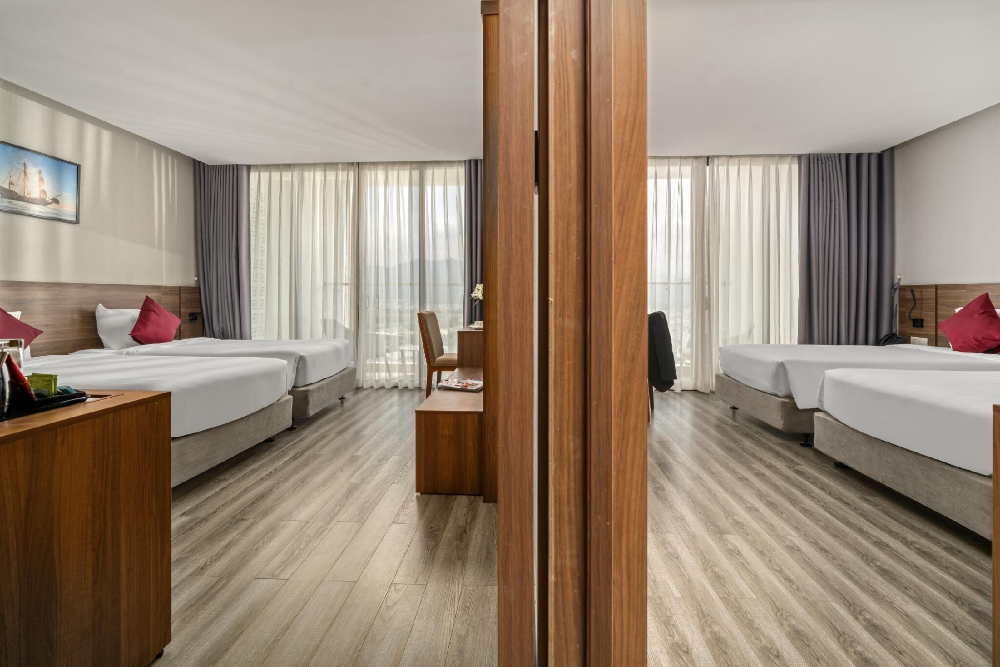 Habitación de hotel con dos camas, un escritorio de madera, una silla y vistas a la ciudad a través de amplios ventanales.