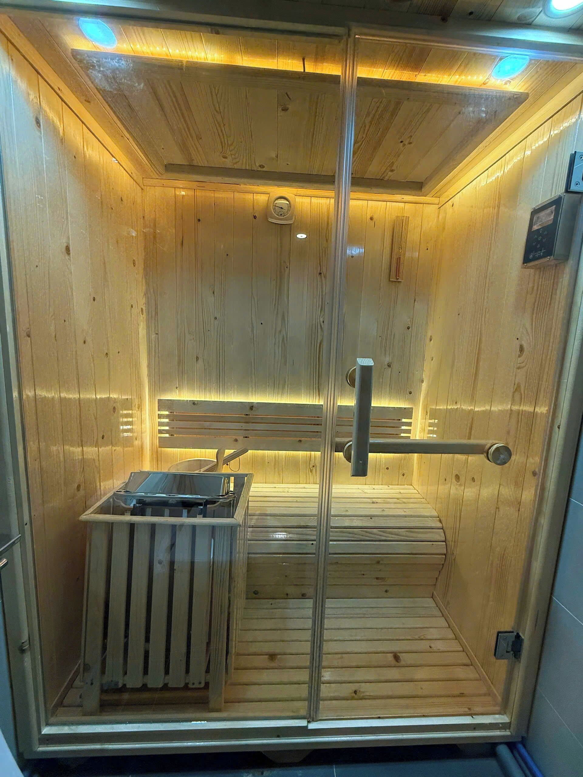 A sauna with wooden walls and a glass door, featuring a bench and a small heater.