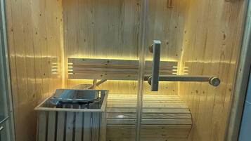 A sauna with wooden walls and a glass door, featuring a bench and a small heater.