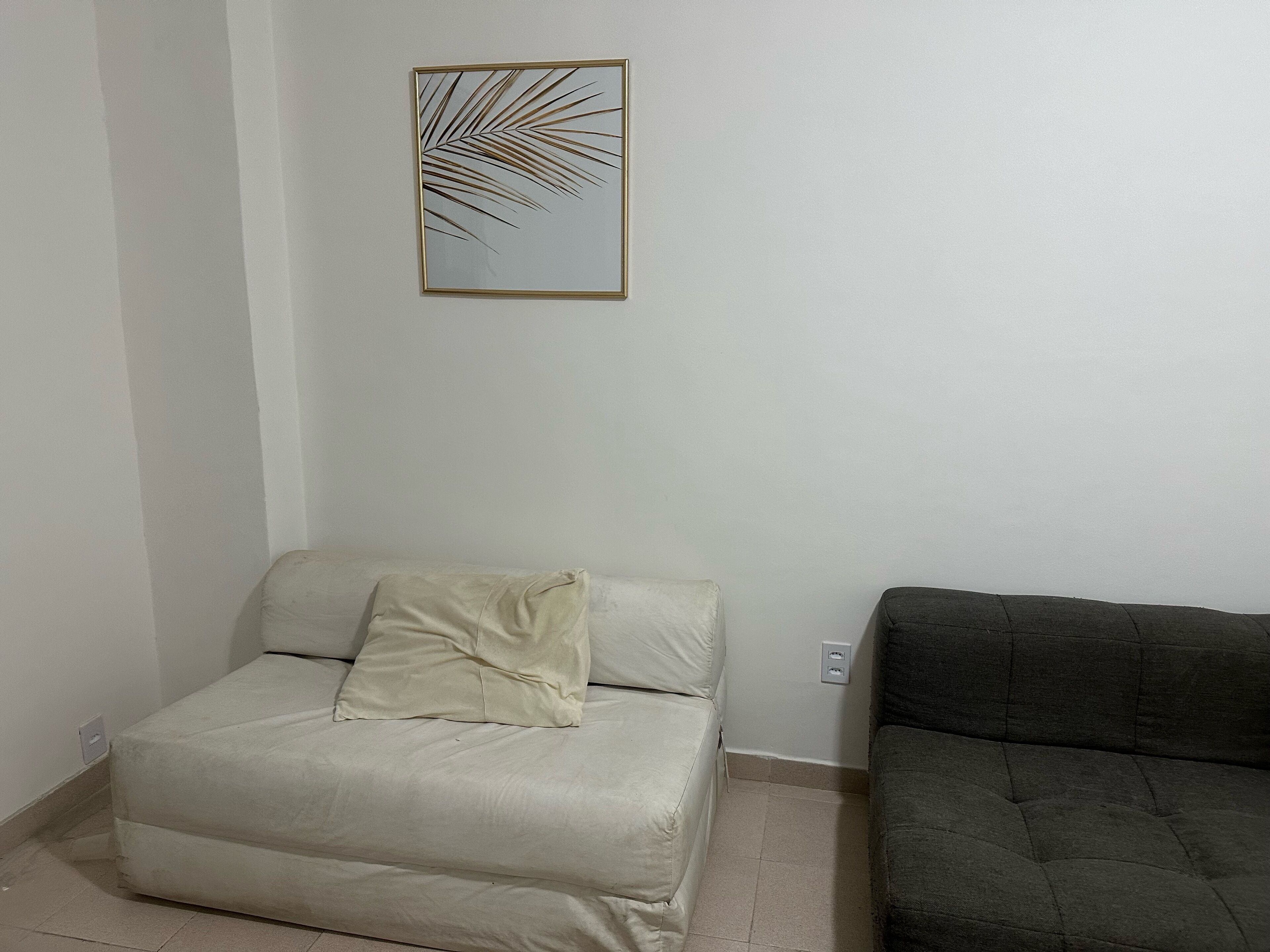 A room with a bed, a gray sofa, and a wall-mounted picture of a palm leaf.