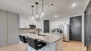 A modern kitchen with a central island, bar stools, stainless steel appliances, pendant lighting, and a grey door. - Serenity I, Luxurious get-away, Pool, WIFI (Princeton)