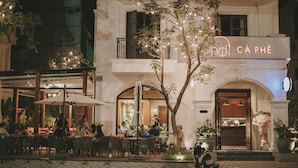 Un edificio con un cartel que dice "HOTEL CÂ PHÊ" y terraza con mesas y sombrillas.